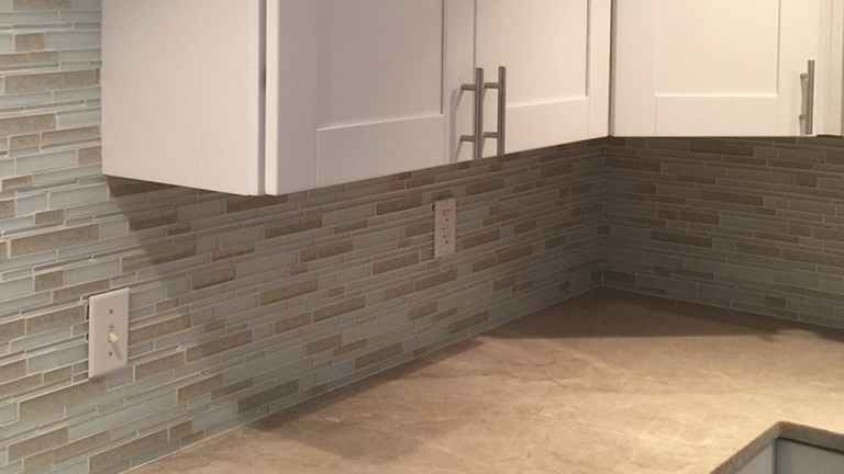 Residential kitchen with a linear glass-and-stone mosaic backsplash and white shaker cabinets